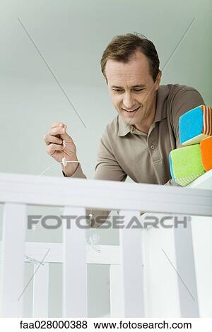 Man leaning over baby crib, holding mobile, looking down View Large Photo Image Stock Photo - Man leaning over baby crib, holding mobile, looking down. Fotosearch