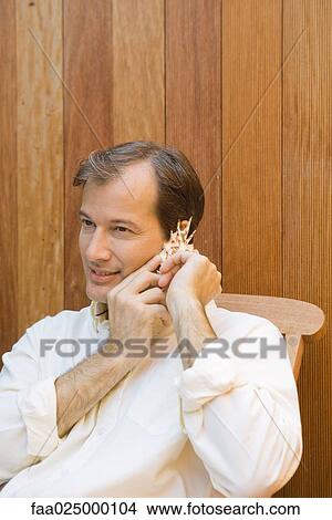 Picture - Man listening to seashell, close-up. Fotosearch