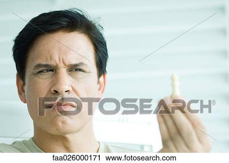Stock Image - Man looking at chess piece, close-up. Fotosearch