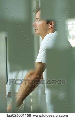 Stock Photograph - Man looking out window, side view, selective focus. Fotosearch