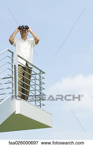 Man looking through binoculars, front view, low angle View Large Photo Image Stock Photo - Man looking through binoculars, front view, low angle. Fotosearch