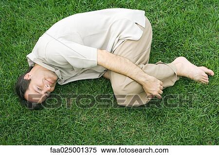 Stock Photography - Man lying in fetal position on grass, smiling up at camera. Fotosearch