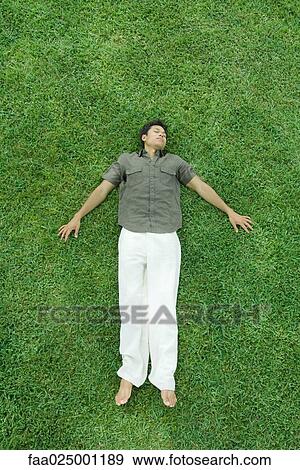Stock Photo - Man lying on back in grass, eyes closed, full length. Fotosearch