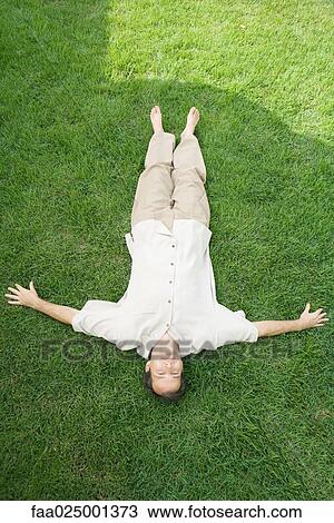 Stock Image - Man lying on back in grass, smiling at camera, high angle view. Fotosearch