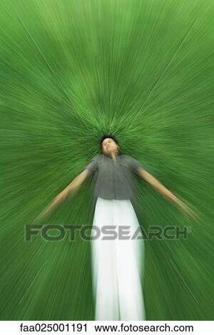 Stock Image - Man lying on back in grass with eyes closed, blurred motion. Fotosearch