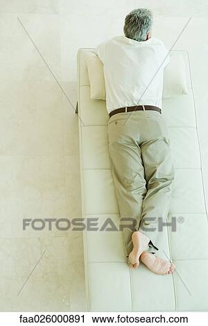 Stock Image - Man lying on stomach on chaise longue, high angle view, full length. Fotosearch