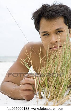 Man lying on the beach touching dune grass, looking at camera View Large Photo Image Stock Image - Man lying on the beach touching dune grass, looking at camera. Fotosearch