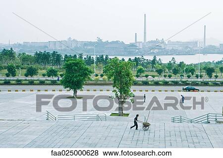Man pushing wheelbarrow in front of city riverscape View Large Photo Image Stock Photo - Man pushing wheelbarrow in front of city riverscape. Fotosearch