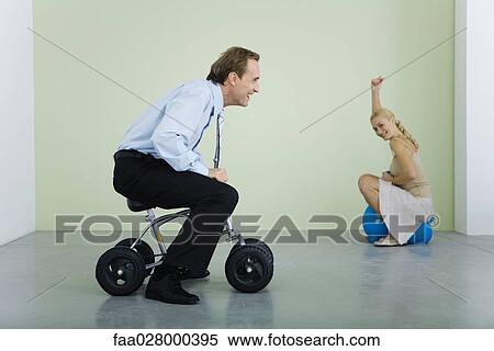 Man riding child's bicycle, woman smiling at camera in background View Large Photo Image Stock Photography - Man riding child's bicycle, woman smiling at camera in background. Fotosearch