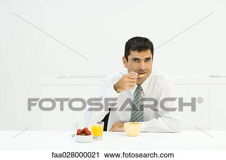 Man sitting at table, eating healthy breakfast, looking at camera View Large Photo Image Stock Image - Man sitting at table, eating healthy breakfast, looking at camera. Fotosearch