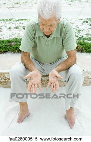 Man sitting at the beach, looking down at hands, high angle view View Large Photo Image Stock Photography - Man sitting at the beach, looking down at hands, high angle view. Fotosearch