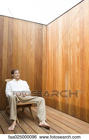 Man sitting in lounge chair, holding coffee mug View Large Photo Image Stock Photograph - Man sitting in lounge chair, holding coffee mug. Fotosearch