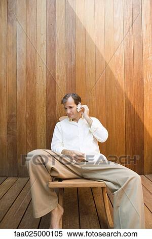 Stock Photography - Man sitting in lounge chair listening to seashell. Fotosearch