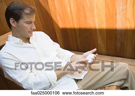 Man sitting in lounge chair looking at sand dollar View Large Photo Image Stock Photograph - Man sitting in lounge chair looking at sand dollar. Fotosearch