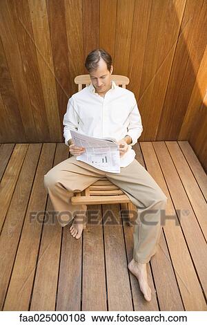 Man sitting in lounge chair reading newspaper, high angle view View Large Photo Image Stock Photo - Man sitting in lounge chair reading newspaper, high angle view. Fotosearch