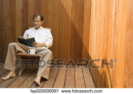 Man sitting in lounge chair with coffee mug, reading book View Large Photo Image Stock Photo - Man sitting in lounge chair with coffee mug, reading book. Fotosearch