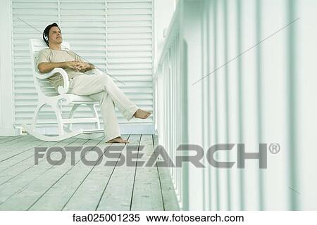 Stock Photography - Man sitting in rocking chair on porch, listening to headphones. Fotosearch
