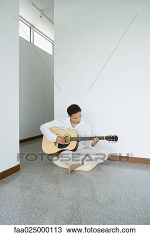 Stock Image - Man sitting on cushion playing acoustic guitar. Fotosearch