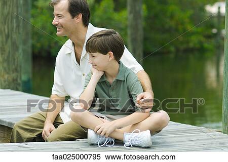 Man sitting on dock with arm around son's shoulder, both looking away and smiling View Large Photo Image Stock Photography - Man sitting on dock with arm around son's shoulder, both looking away and smiling. Fotosearch