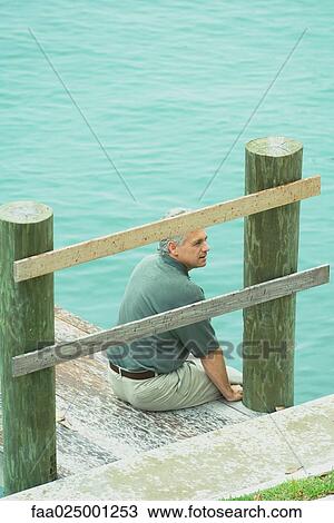 Man sitting on edge of dock, looking away, high angle view View Large Photo Image Stock Image - Man sitting on edge of dock, looking away, high angle view. Fotosearch