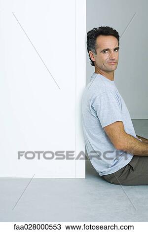 Man sitting on floor, leaning against wall, smiling at camera View Large Photo Image Stock Image - Man sitting on floor, leaning against wall, smiling at camera. Fotosearch