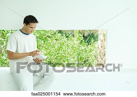 Man sitting on ledge reading book View Large Photo Image Picture - Man sitting on ledge reading book. Fotosearch