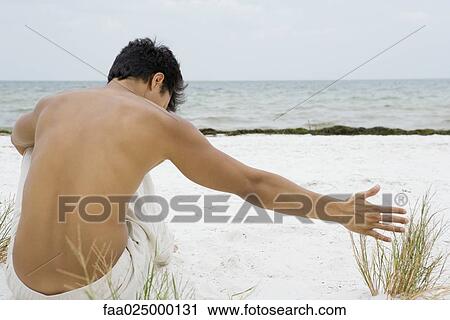 Man sitting on the beach touching dune grass, rear view View Large Photo Image Stock Image - Man sitting on the beach touching dune grass, rear view. Fotosearch