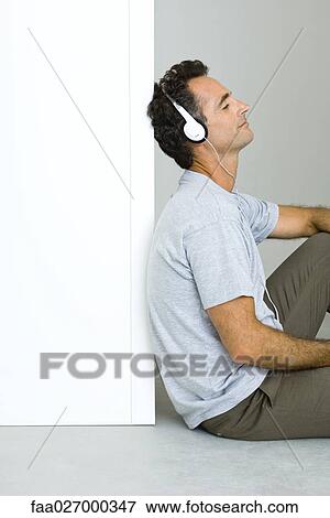 Man sitting on the ground, listening to headphones, eyes closed View Large Photo Image Stock Photo - Man sitting on the ground, listening to headphones, eyes closed. Fotosearch