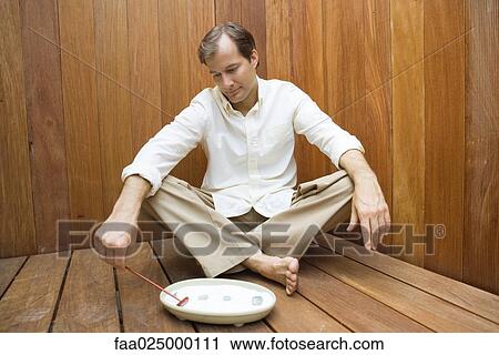 Stock Image - Man sitting on the ground raking rock garden. Fotosearch