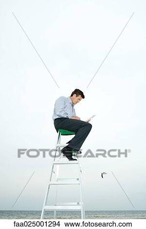 Man sitting on top of ladder, using laptop View Large Photo Image Picture - Man sitting on top of ladder, using laptop. Fotosearch