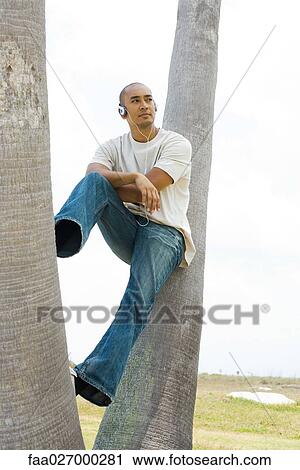 Man sitting on tree trunk, listening to headphones, looking away View Large Photo Image Stock Image - Man sitting on tree trunk, listening to headphones, looking away. Fotosearch