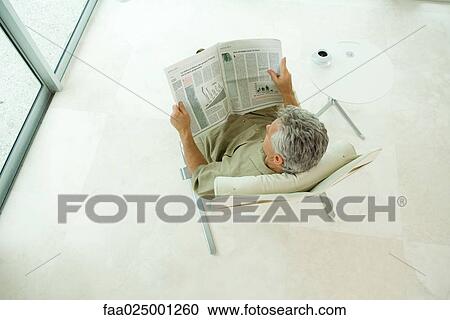 Stock Image - Man sitting, reading newspaper, high angle view. Fotosearch