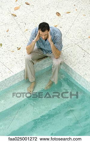 Man sitting with feet in pool, holding head, high angle view View Large Photo Image Stock Image - Man sitting with feet in pool, holding head, high angle view. Fotosearch