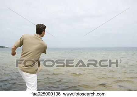 Man skimming stones at the beach, rear view View Large Photo Image Stock Photograph - Man skimming stones at the beach, rear view. Fotosearch