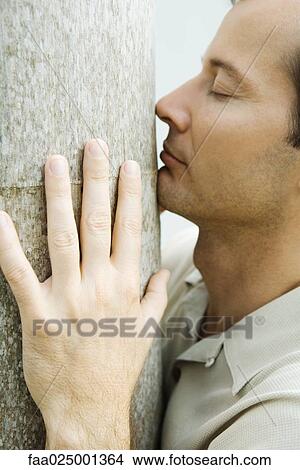 Picture - Man smelling tree trunk, eyes closed, close-up. Fotosearch