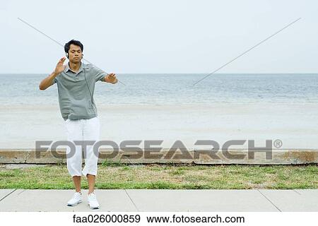 Man standing at the beach with arms out, listening to headphones, eyes closed View Large Photo Image Stock Photo - Man standing at the beach with arms out, listening to headphones, eyes closed. Fotosearch
