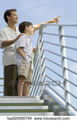 Man standing at top of staircase with son and pointing at sky, low angle view View Large Photo Image Picture - Man standing at top of staircase with son and pointing at sky, low angle view. Fotosearch