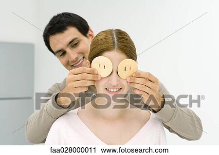 Man standing behind woman, covering her eyes with cookies, both smiling View Large Photo Image Stock Image - Man standing behind woman, covering her eyes with cookies, both smiling. Fotosearch