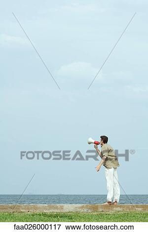Man standing by the sea, shouting into megaphone, side view View Large Photo Image Stock Photo - Man standing by the sea, shouting into megaphone, side view. Fotosearch