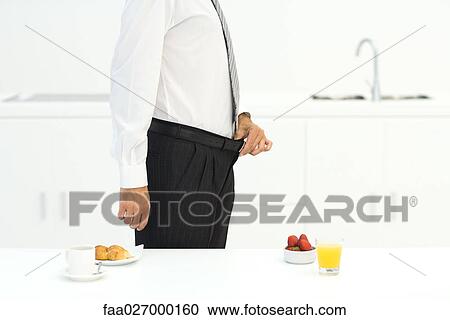 Man standing in kitchen beside two breakfast options, holding waistline of pants, cropped View Large Photo Image Stock Image - Man standing in kitchen beside two breakfast options, holding waistline of pants, cropped. Fotosearch
