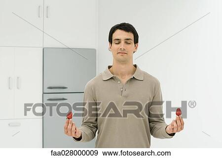 Man standing in kitchen with eyes closed, holding strawberry in each hand View Large Photo Image Stock Photo - Man standing in kitchen with eyes closed, holding strawberry in each hand. Fotosearch