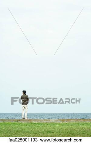 Man standing, looking out toward sea, full length, rear view View Large Photo Image Stock Image - Man standing, looking out toward sea, full length, rear view. Fotosearch