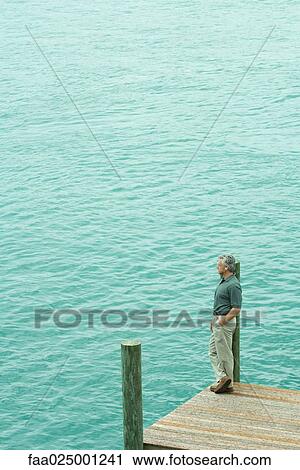 Man standing next to water listening to earphones, looking away, high angle view View Large Photo Image Stock Image - Man standing next to water listening to earphones, looking away, high angle view. Fotosearch