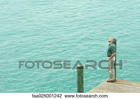 Man standing next to water listening to earphones, looking away, high angle view View Large Photo Image Stock Image - Man standing next to water listening to earphones, looking away, high angle view. Fotosearch