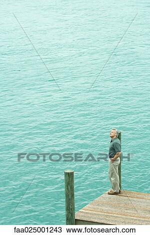 Man standing next to water listening to earphones, looking up, high angle view View Large Photo Image Stock Image - Man standing next to water listening to earphones, looking up, high angle view. Fotosearch