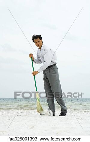 Man standing on beach sweeping with broom, looking at camera View Large Photo Image Stock Image - Man standing on beach sweeping with broom, looking at camera. Fotosearch
