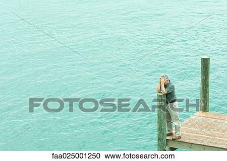 Man standing on dock, leaning on post, holding head, high angle view View Large Photo Image Stock Image - Man standing on dock, leaning on post, holding head, high angle view. Fotosearch