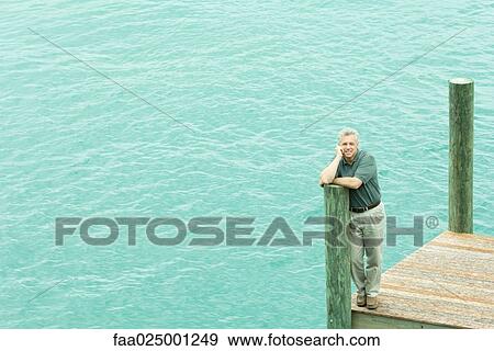 Man standing on dock, leaning on post, smiling at camera, high angle view View Large Photo Image Stock Photo - Man standing on dock, leaning on post, smiling at camera, high angle view. Fotosearch