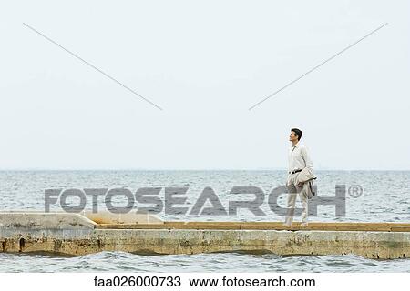 Man standing on jetty, looking at sea, in mid distance View Large Photo Image Stock Image - Man standing on jetty, looking at sea, in mid distance. Fotosearch