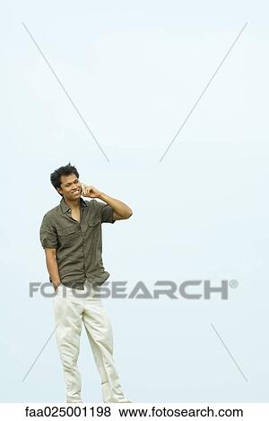 Man standing, using cell phone, body of water in background View Large Photo Image Stock Photo - Man standing, using cell phone, body of water in background. Fotosearch